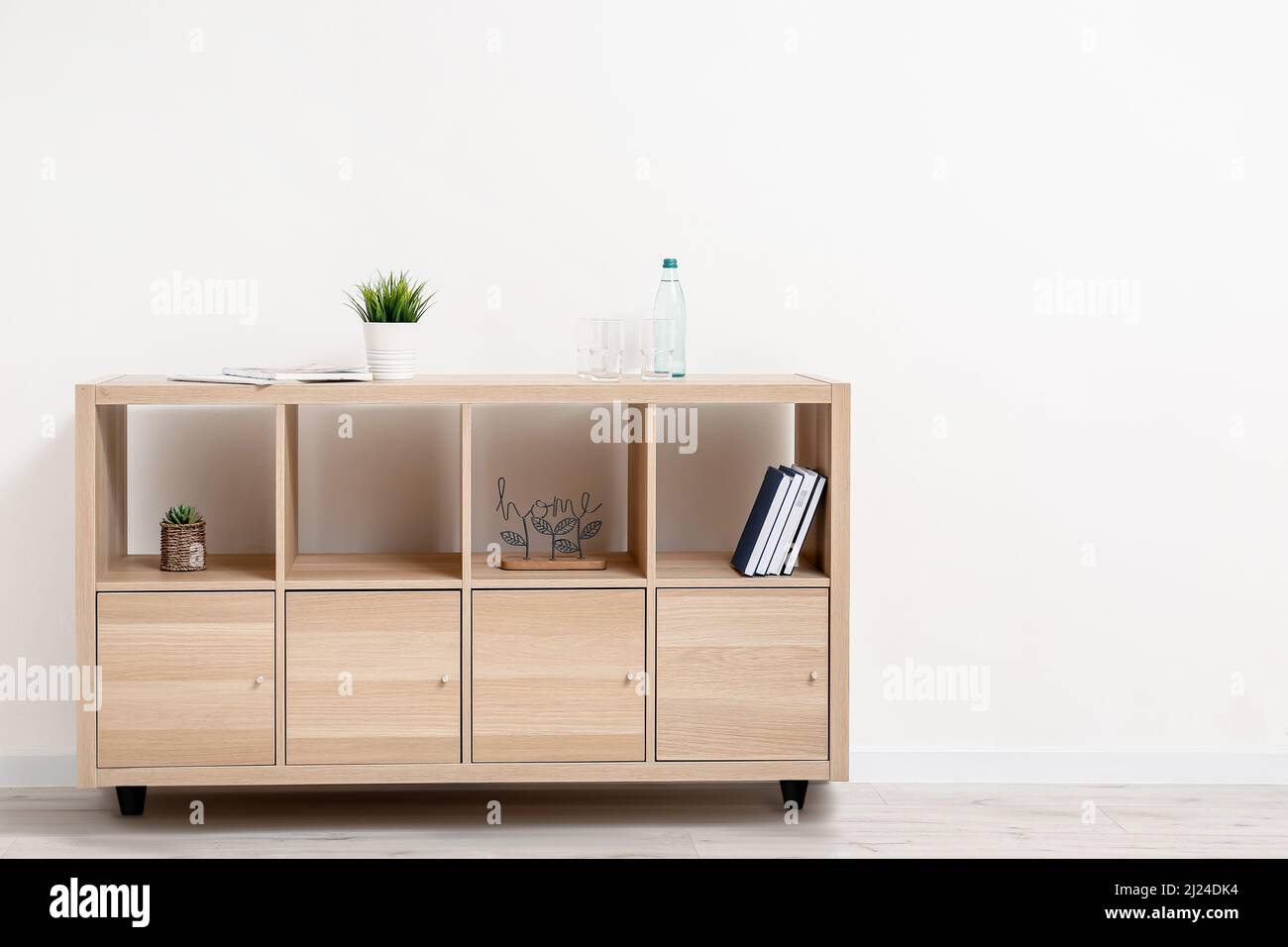 Shelving unit with bottle of water and glasses near light wall Stock