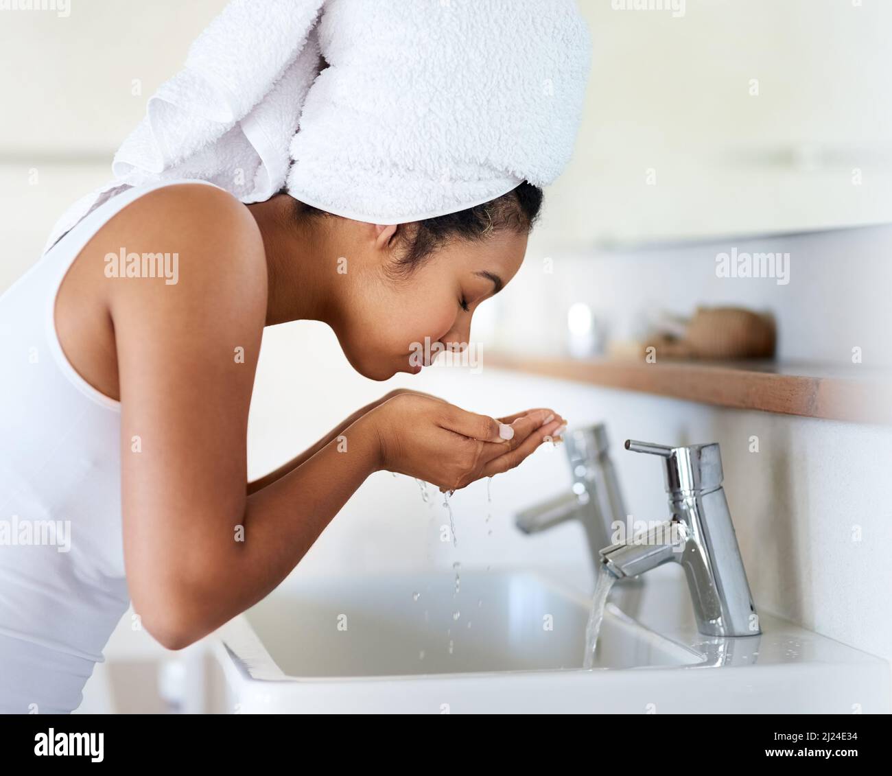 My skin care routine. Shot of a young woman washing her face at the bathroom sink. Stock Photo