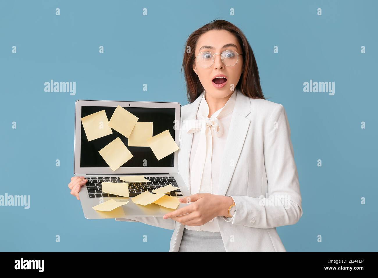 Surprised young woman with sticky note papers on laptop against blue background Stock Photo