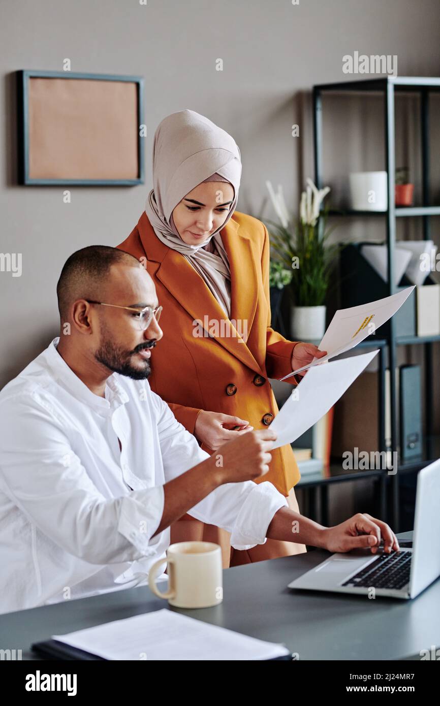 Young secretary in hijab and orange jacket consulting with her male ...