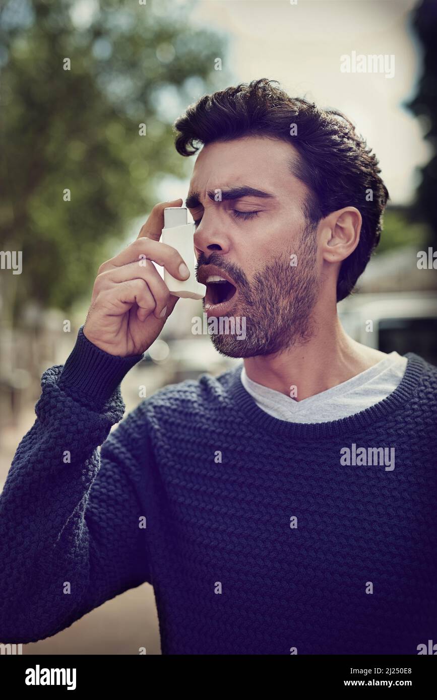 Getting his symptoms under control. Cropped shot of a young man using his asthma pump outside. Stock Photo