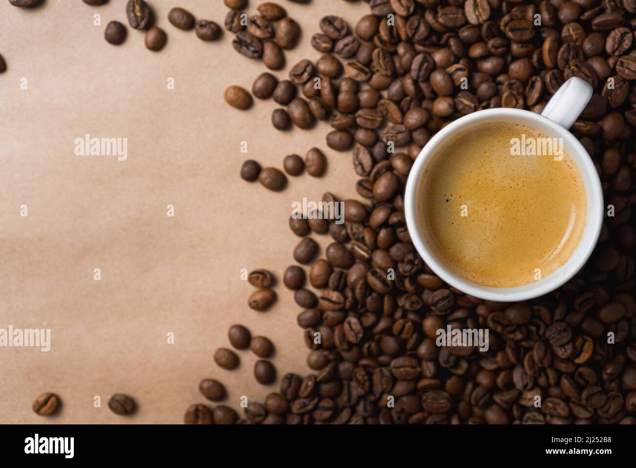Small white coffee cup with espresso crema on roasted beans at brown