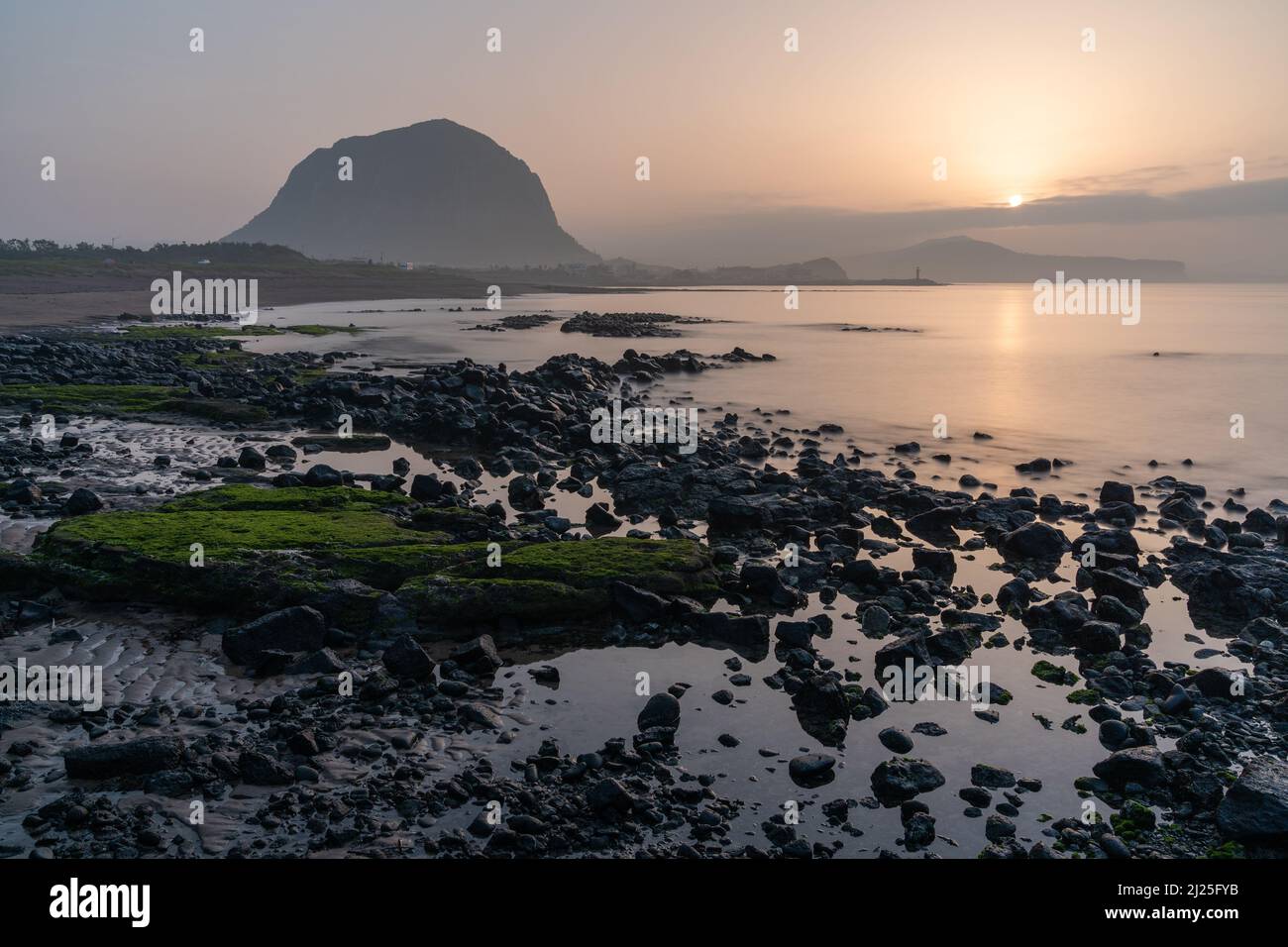 Sunrise over Sagye Beach at low tide, with the volcanic oreum Sangbansan rising behind, an iconic sight on Jeju Island, South Korea Stock Photo