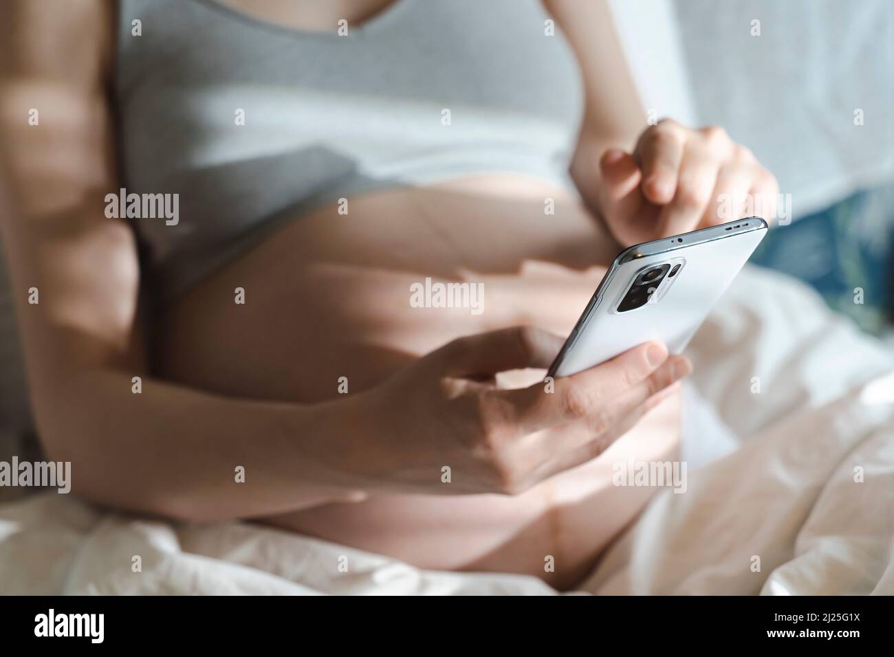 A pregnant woman uses a smartphone while relaxing in her home bed. Internet, shopping, communication during pregnancy and before the birth of a child. Women's and newborn health. High quality photo Stock Photo