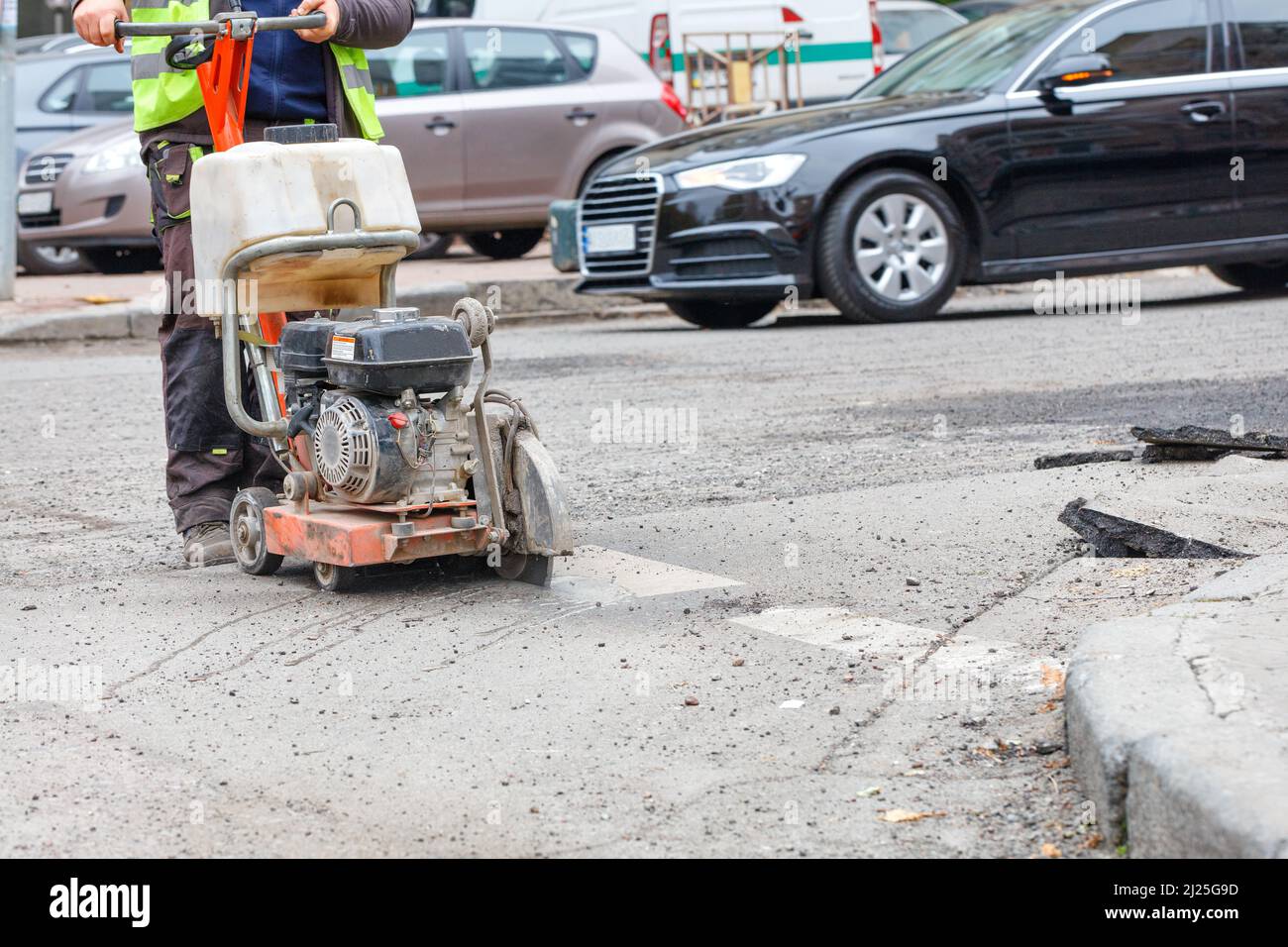 A petrol cutter cuts old asphalt with a diamond wheel, a road worker repairs the carriageway of a city road. Stock Photo
