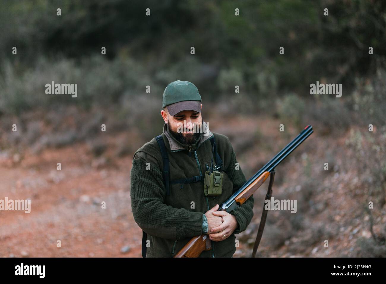 Portrait of hunting man holding his shotgun and smiling as he looks down Stock Photo