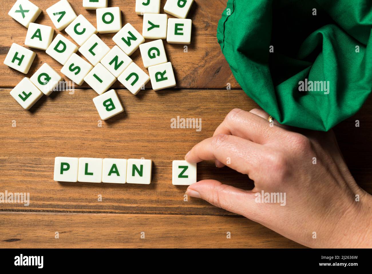 A hand placing a piece with the letter Z next to the word PLAN. An empty green bag and other pieces with letters appear displaced. Concept of planning Stock Photo