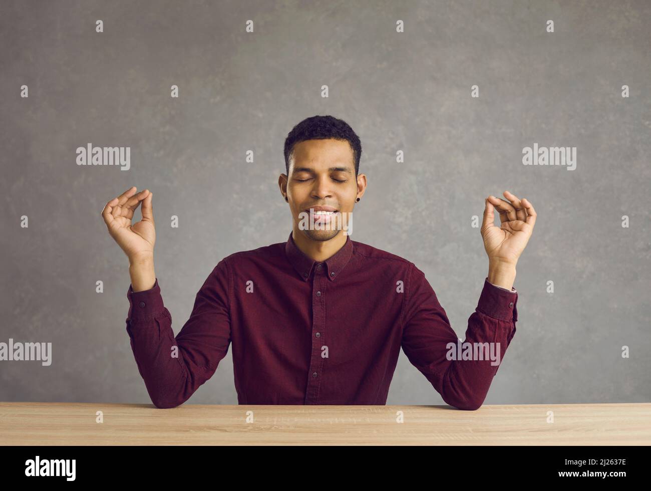 Happy calm young latin man meditating with eyes closed smiling sitting at desk. Stock Photo