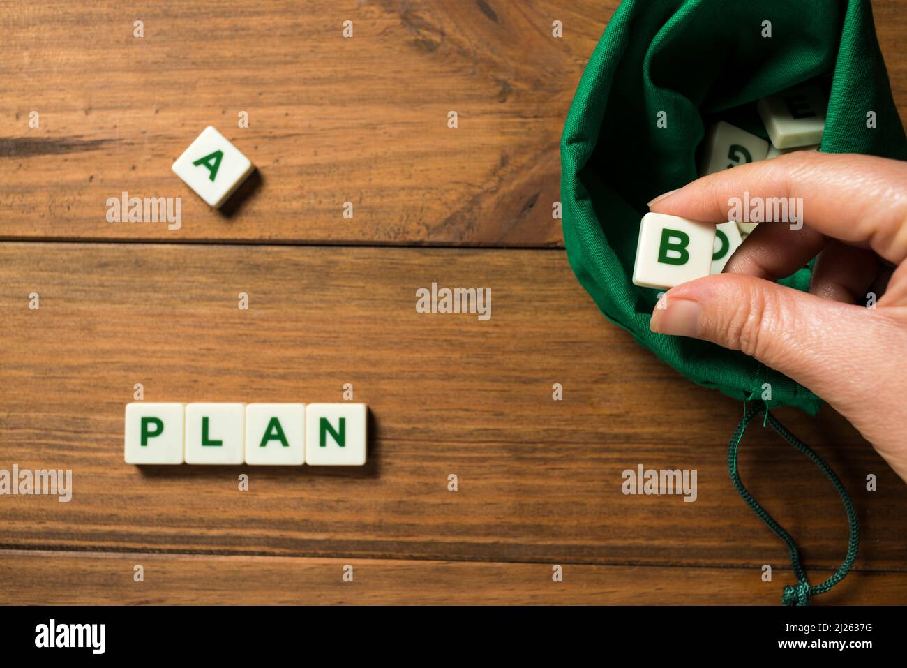 A hand taking out a piece with the letter B out of a green bag full of lettered pieces, to form the sentence PLAN B. Concept of planning for the futur Stock Photo