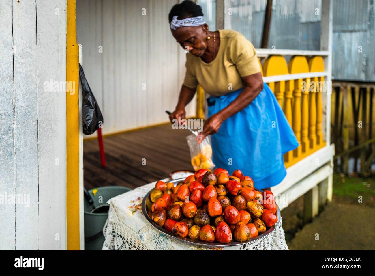 An Afro-Colombian woman salts freshly cooked chontaduro (peach palm) fruits on the porch of her house in Quibdó, Chocó, Colombia. Stock Photo