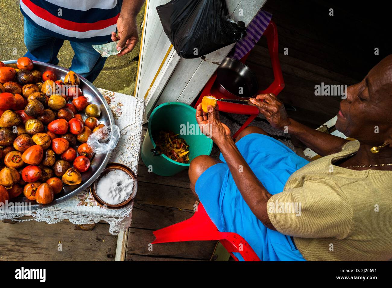 An Afro-Colombian woman salts freshly cooked chontaduro (peach palm) fruits on the porch of her house in Quibdó, Chocó, Colombia. Stock Photo