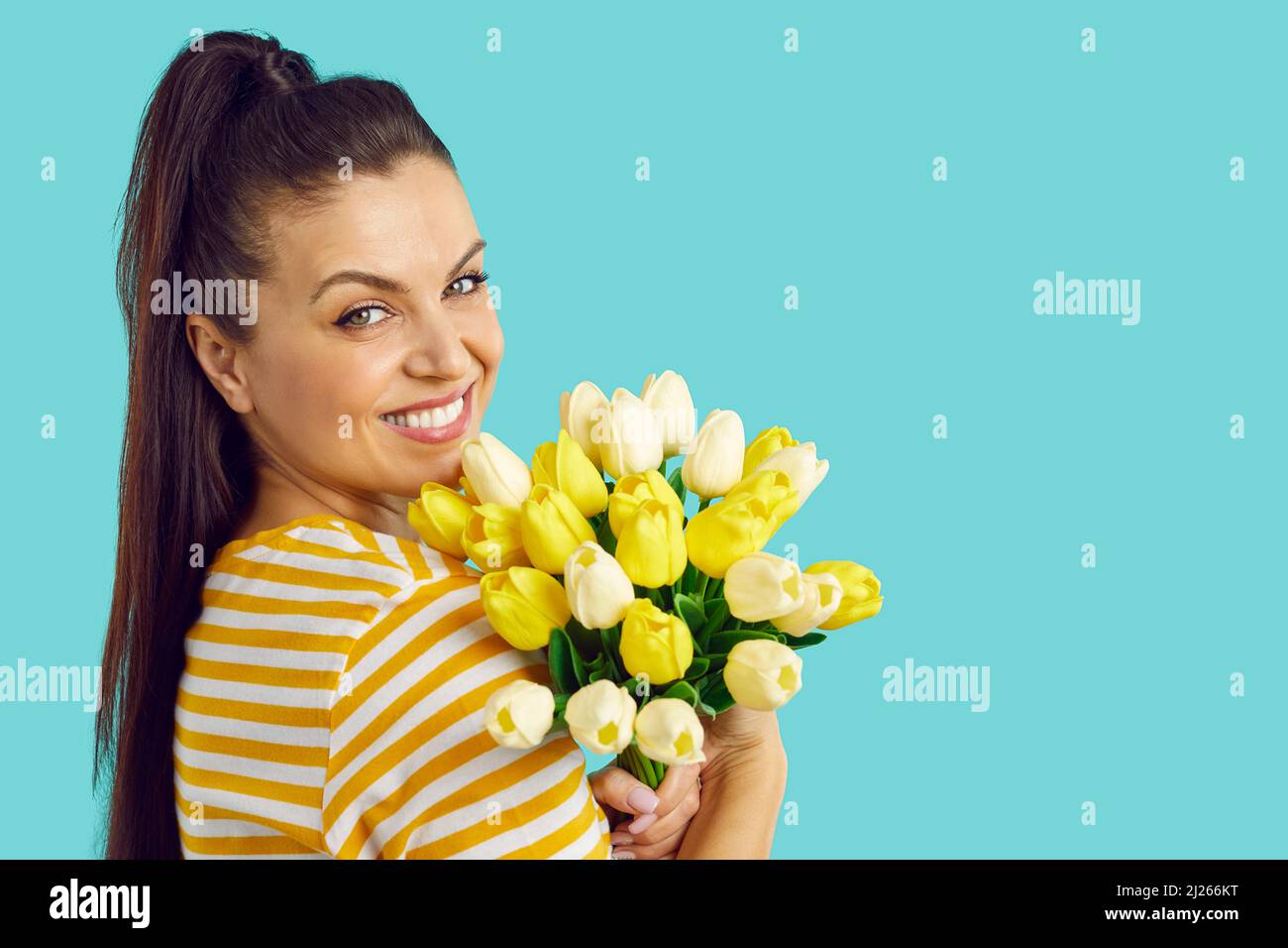 Portrait of a cheerful young woman with a bouquet of yellow tulips isolated on blue background. Cute girl smiling on blank wall background, copy space Stock Photo