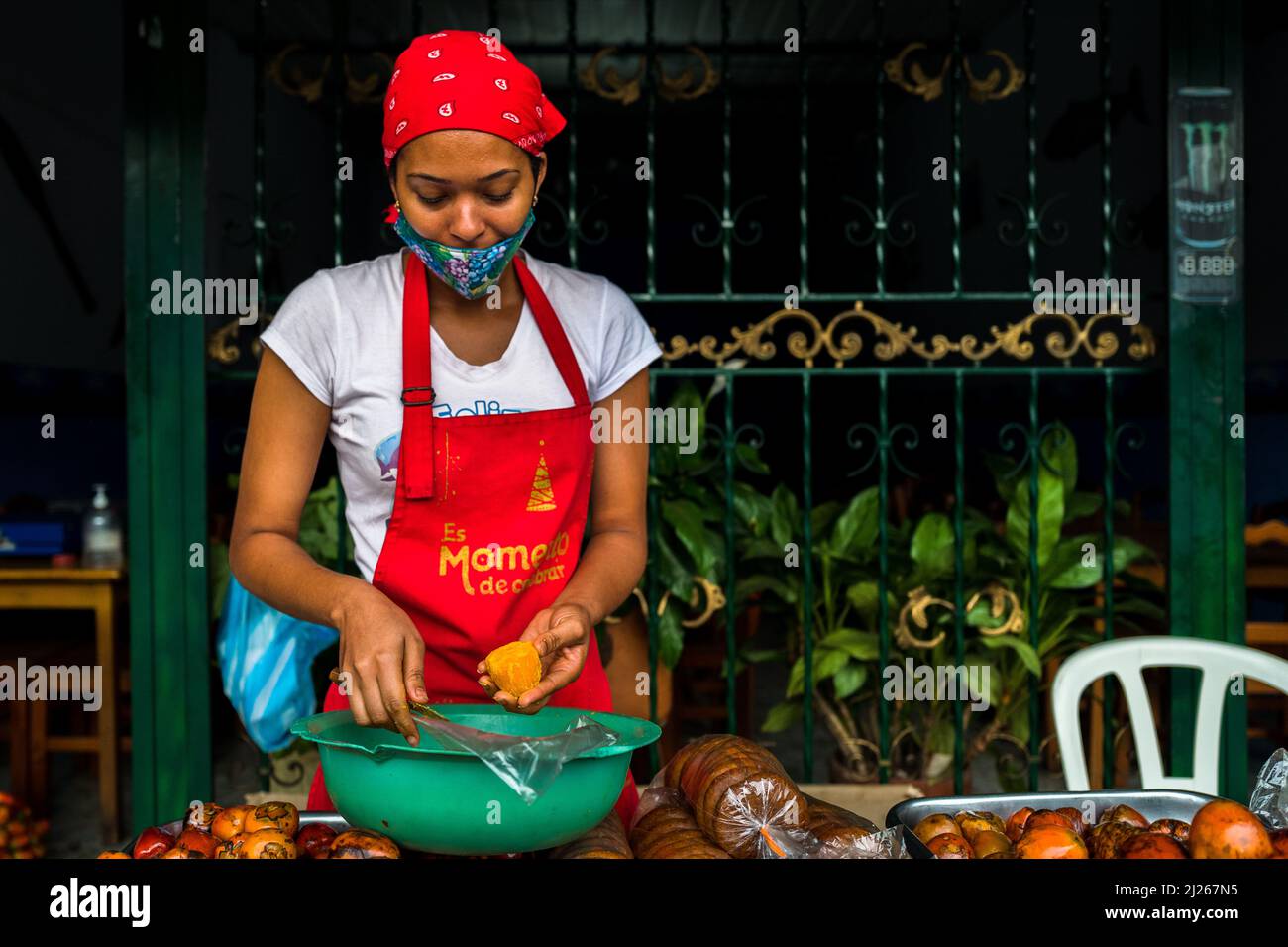 An Afro-Colombian woman peels a freshly cooked chontaduro (peach palm) fruit in a street restaurant in Cali, Valle del Cauca, Colombia. Stock Photo