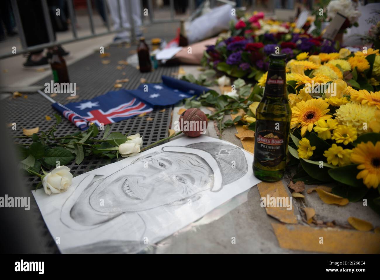 Melbourne, Australia. 30th March 2022. A portrait of Shane Warne sits beneath his statue among flowers and beer before the memorial service commemorating his life. Credit: Jay Kogler/Alamy Live News Stock Photo