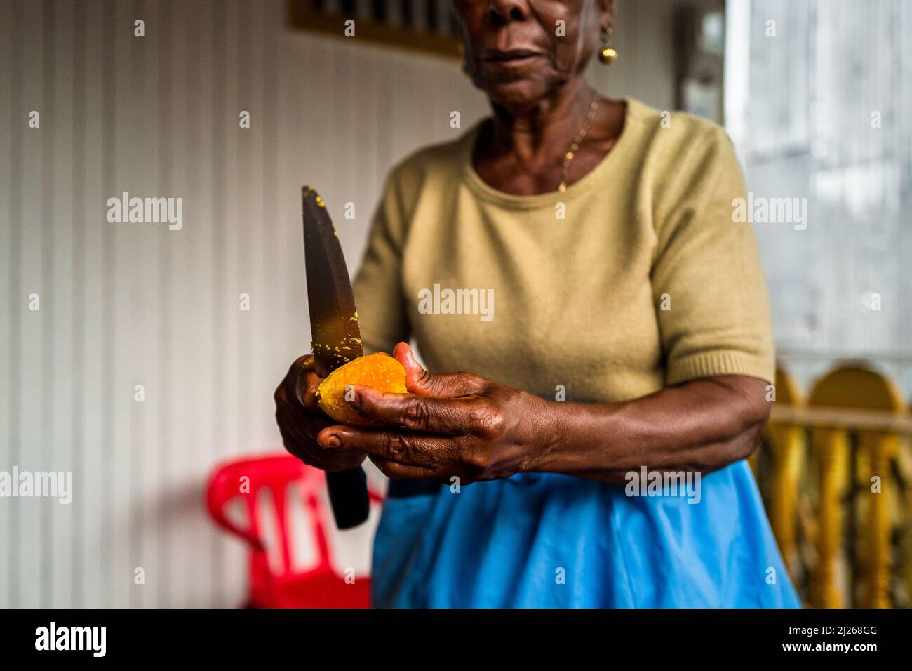 An Afro-Colombian woman peels a freshly cooked chontaduro (peach palm) fruit with a knife on the porch of her house in Quibdó, Chocó, Colombia. Stock Photo
