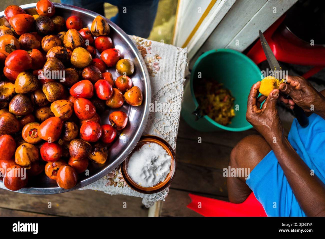 An Afro-Colombian woman peels a freshly cooked chontaduro (peach palm) fruit with a knife on the porch of her house in Quibdó, Chocó, Colombia. Stock Photo