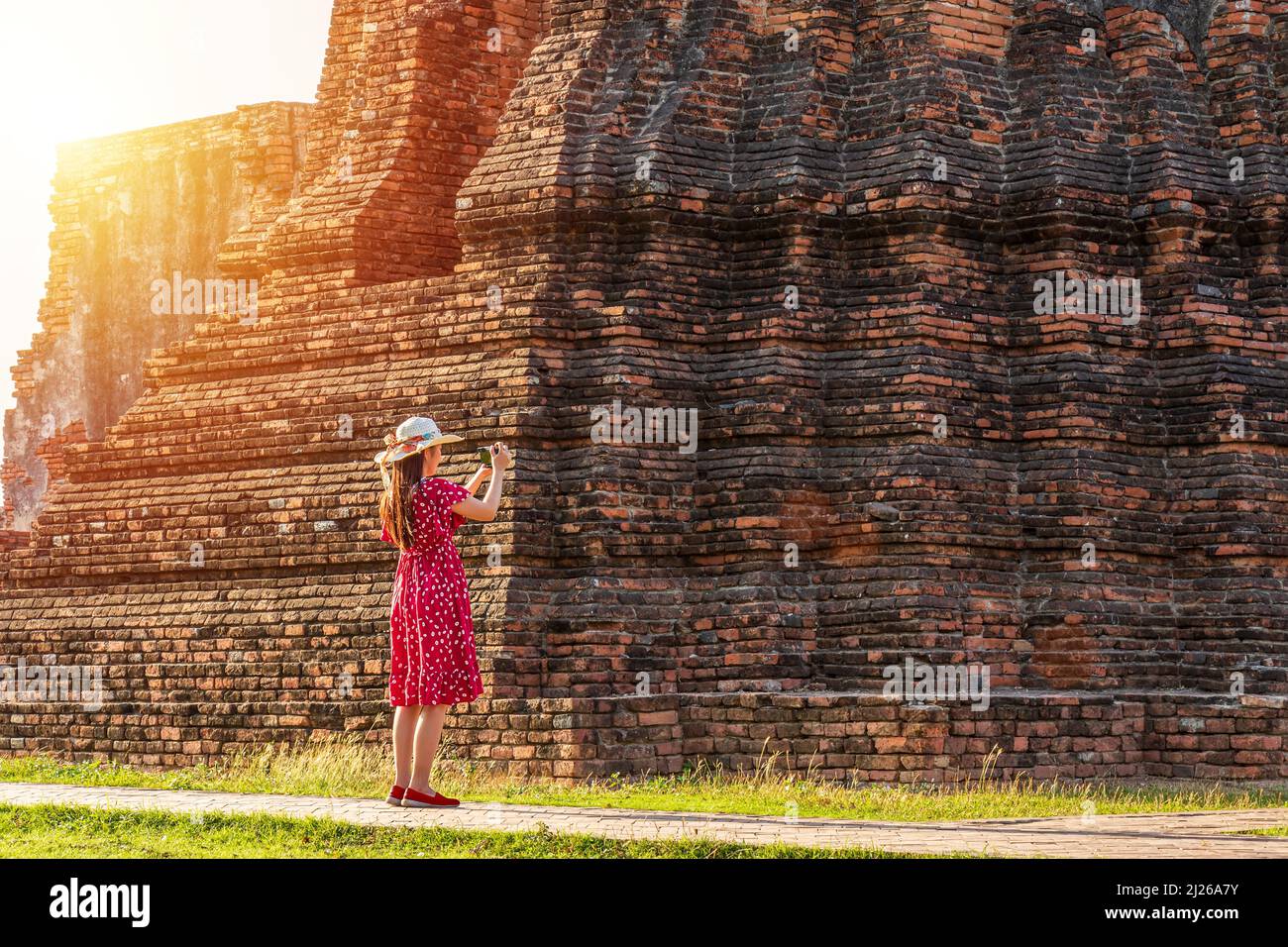 solo traveler concept. happy Asian woman tourist in red dress taking picture of old pagoda around history temple for cultural tourism at Ayutthaya Stock Photo