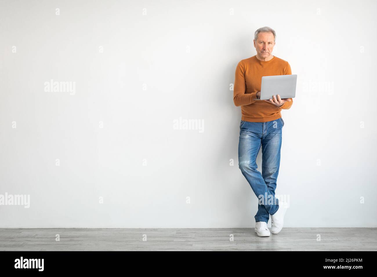 Confident mature man using laptop leaning on wall Stock Photo