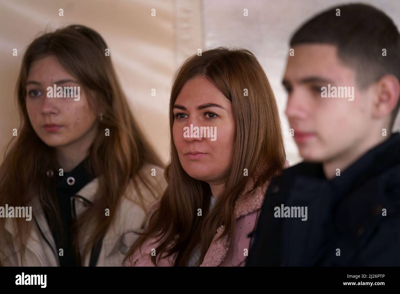 A family of Ukrainian refugees, Viktoria Artemenko (centre) and her children Violetta and Vitaliy, sit outside temporary accommodation in Przemysl, Poland, as they wait for news of their UK visa application after being matched with a family in Manchester. The family are being assisted by a Bristol-based charity, Love Bristol, who have helped around 70 Ukrainian refugees in Poland apply for UK visas, and say that none so far have been approved in the thirteen days since the sponsorship scheme opened for applications. Picture date: Wednesday March 30, 2022. Stock Photo