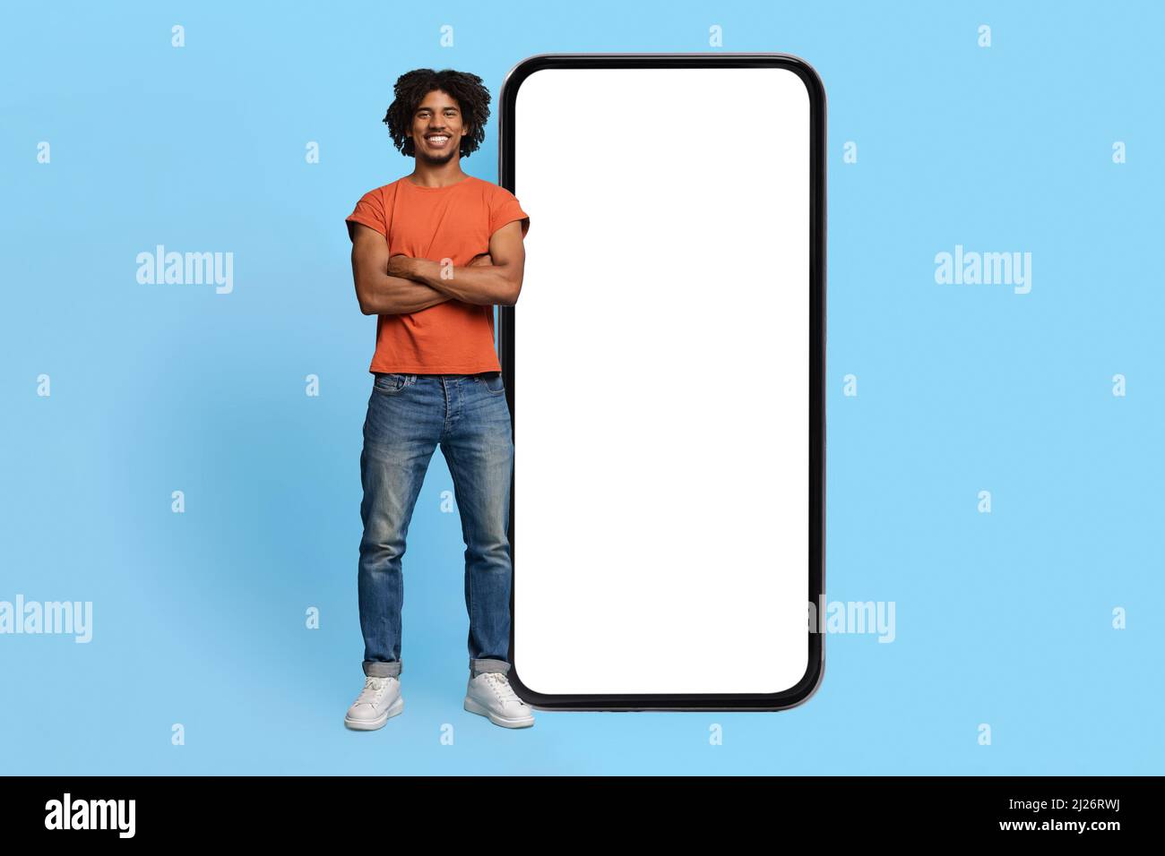 Confident black guy posing by big smartphone with empty screen Stock Photo