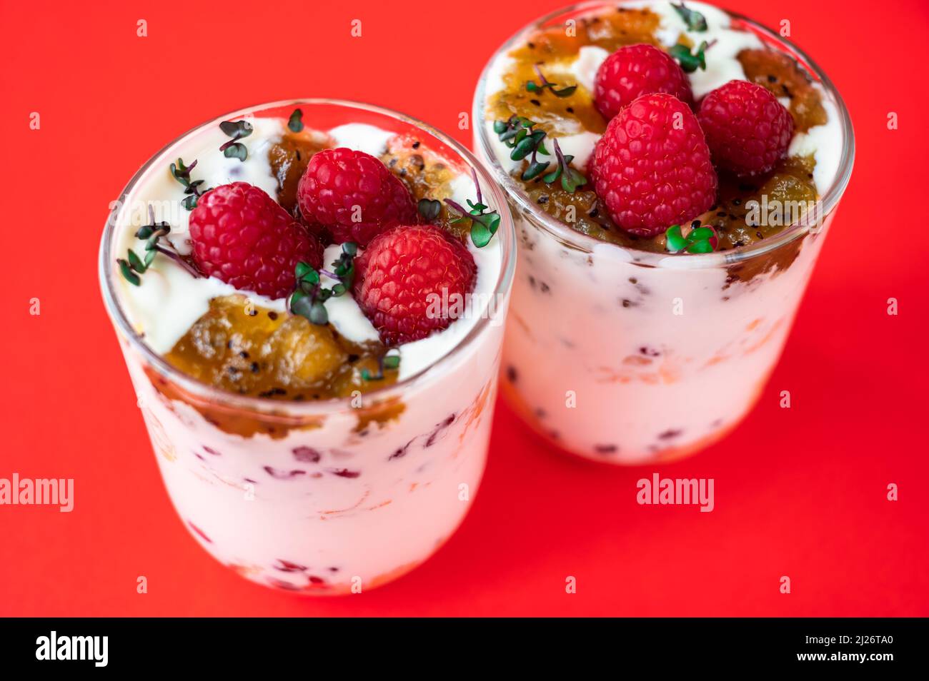 Two glass with coconut mousse with raspberry, kiwi jam and tiny herb leaf on red background, closeup. Stock Photo