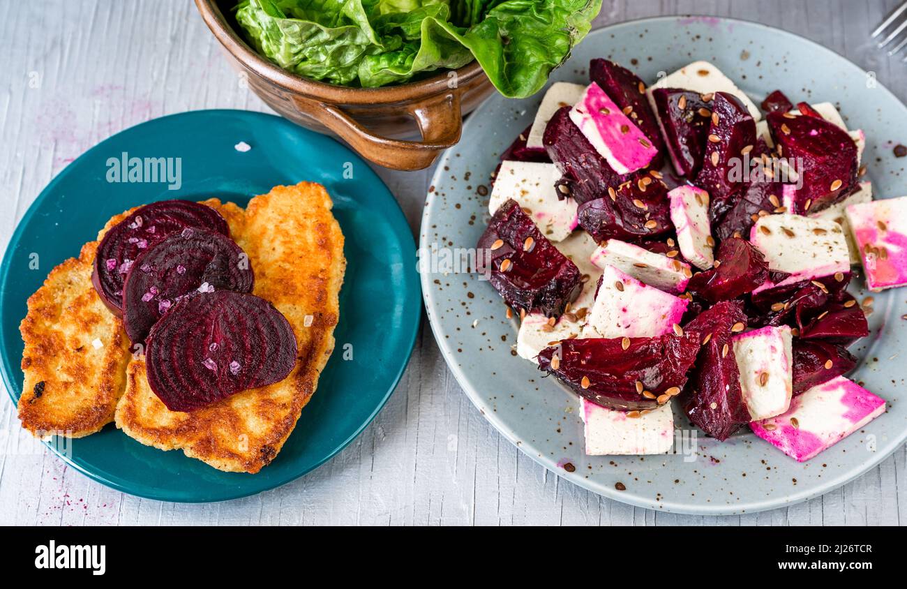 Fried breaded celery and red beetroot, tofu salad with red beetroot and flaxseed, lettuce salad on plates on table, closeup. Healthy vegetarian or veg Stock Photo