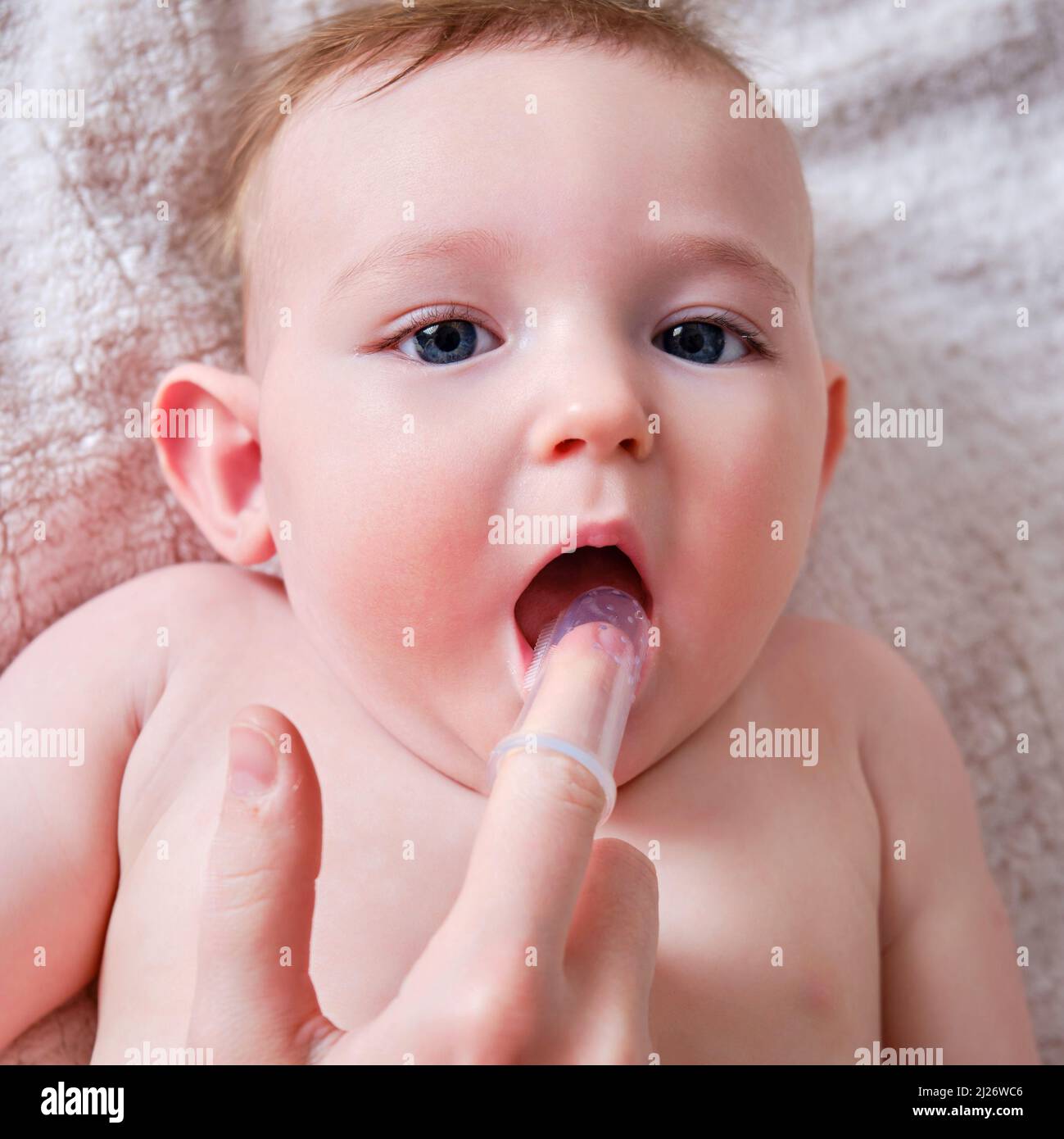 Mother hands brushing teeth with a finger brush of a happy infant baby