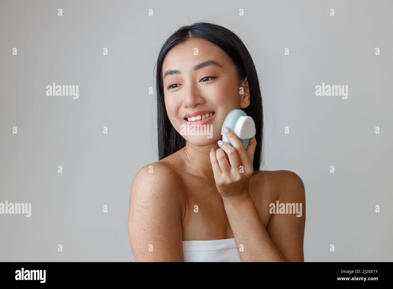 Cheerful Asian woman massaging cheek with face massager Stock Photo