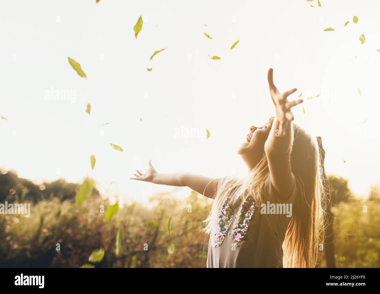 Happy little blonde girl plays with green leaves in garden, field. The ...