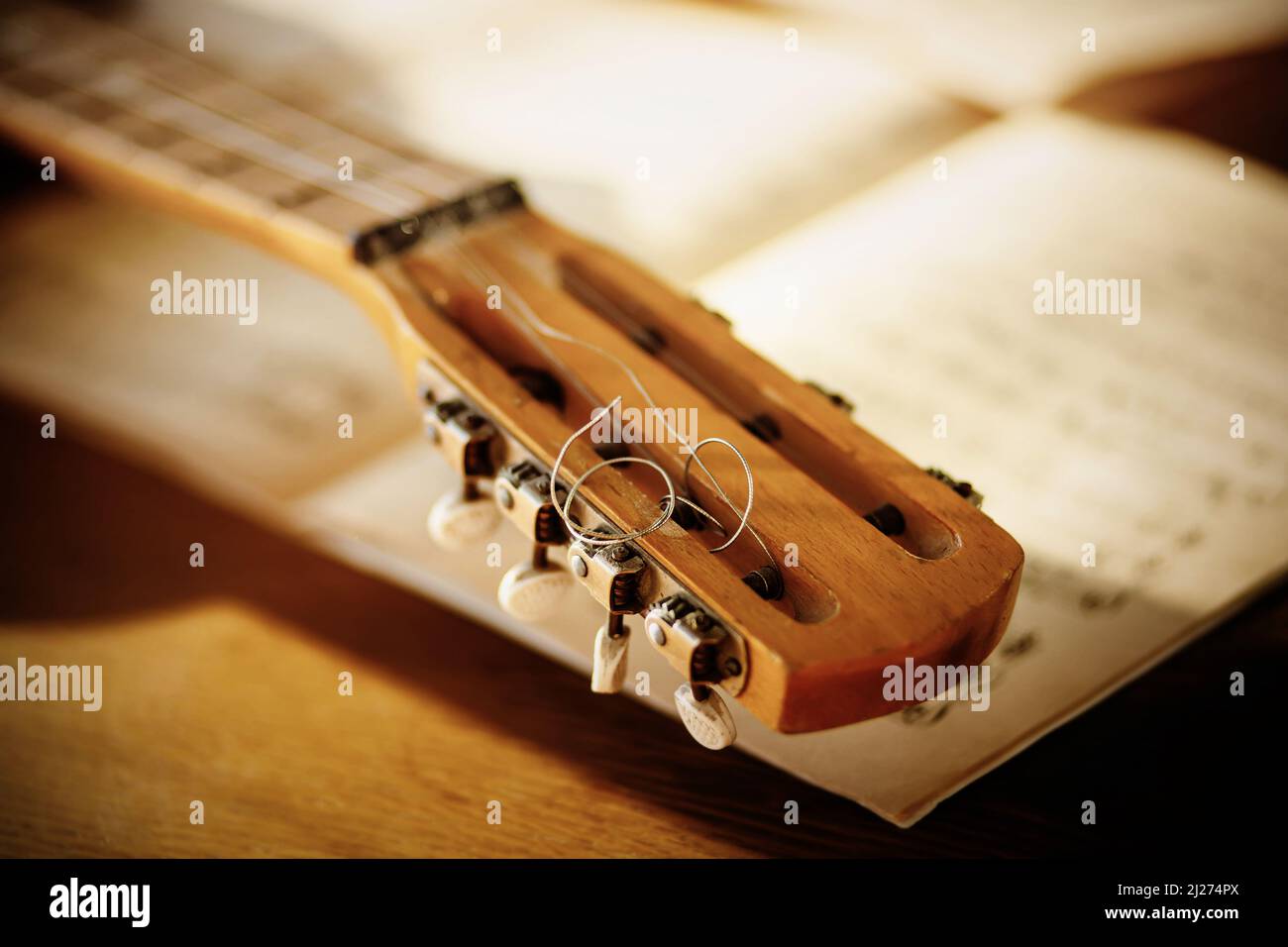 The fretboard of an old vintage acoustic guitar with metal strings lying on a wooden table next to sheets of sheet music. Solfeggio and music lessons Stock Photo