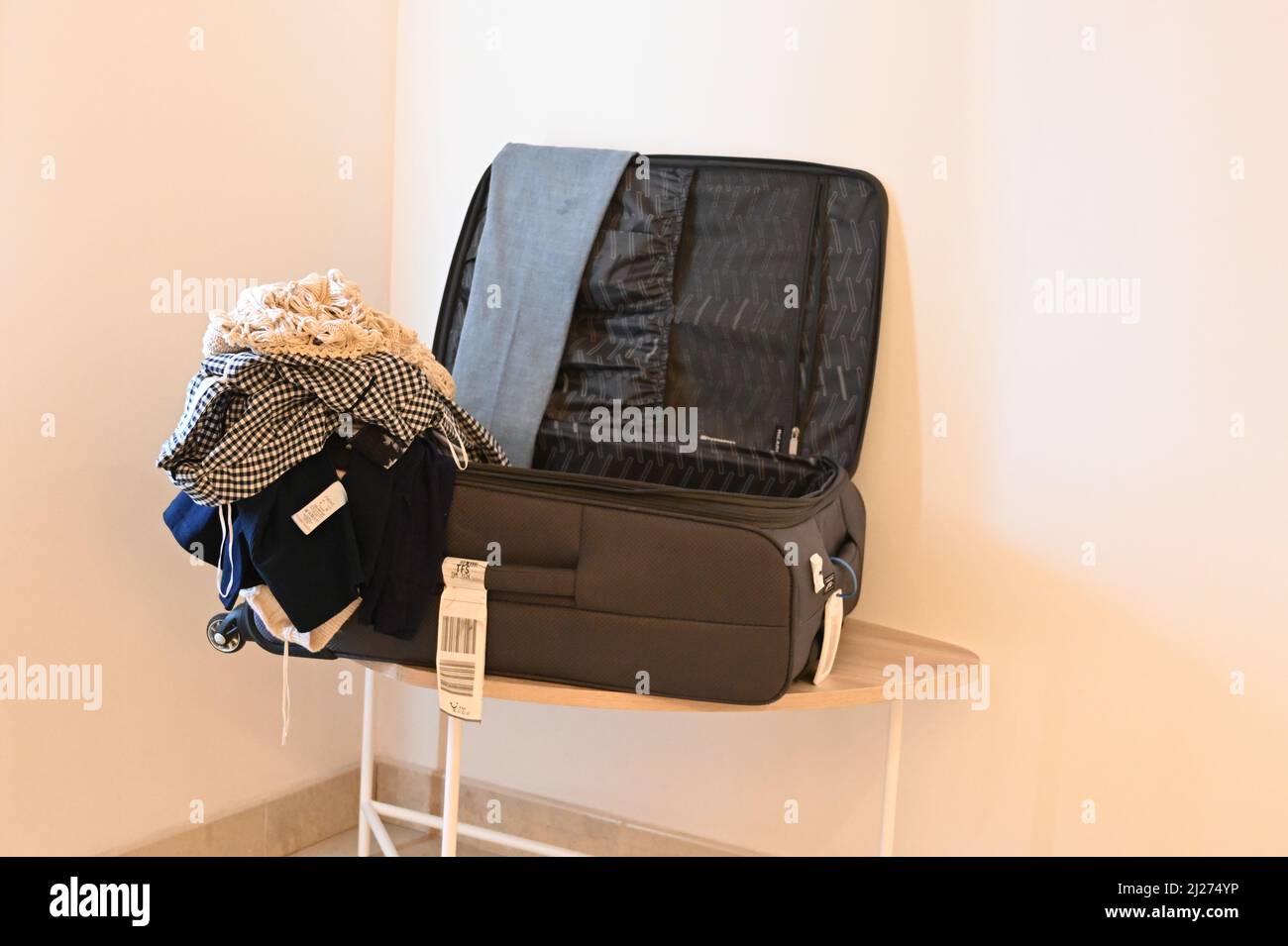 An open suitcase in a hotel suite sitting on a table, open, with clothes piled up on the side. Stock Photo