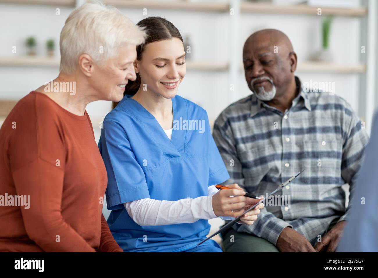 Cheerful young woman doctor having conversation with senior people ...