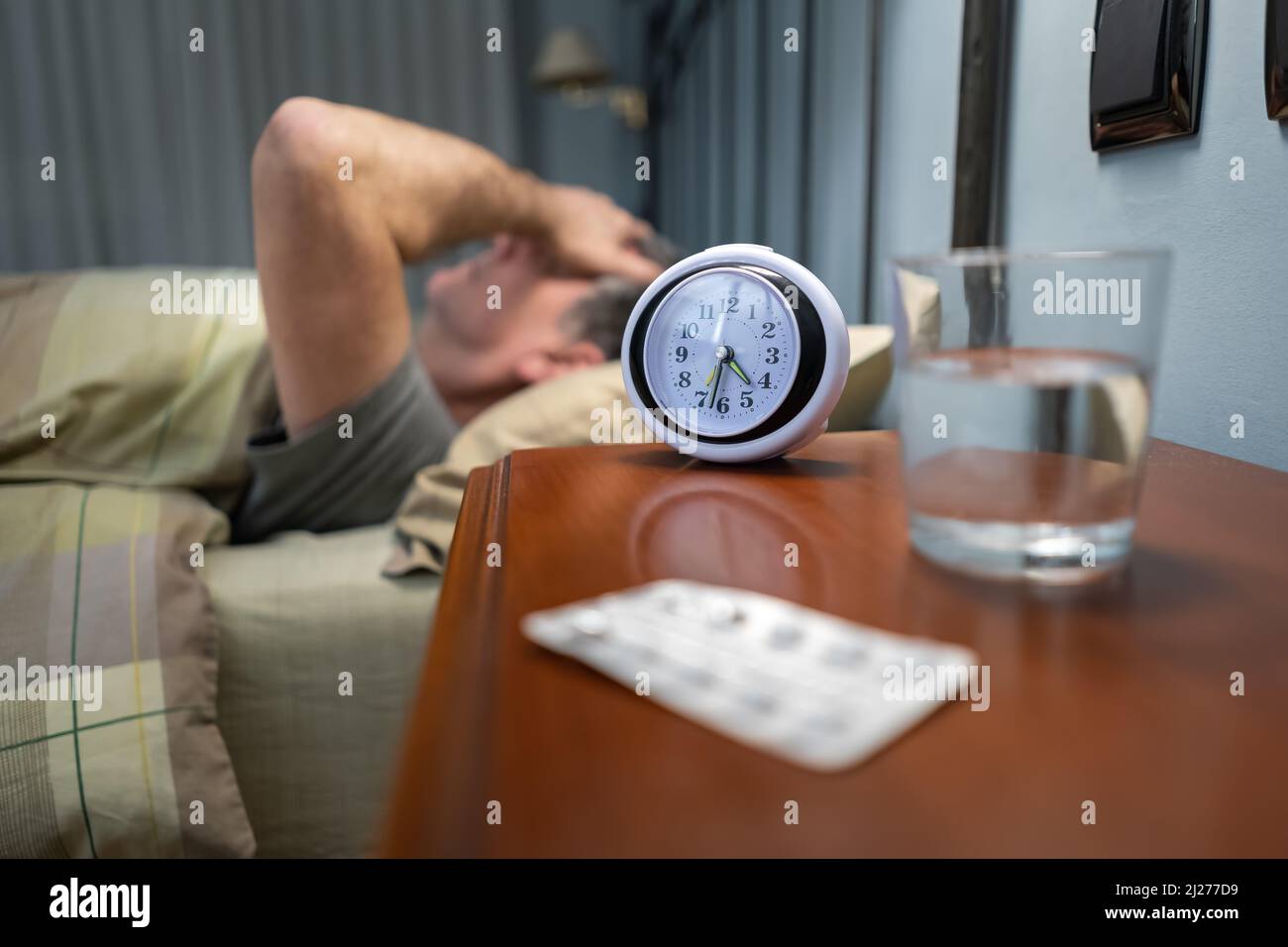 Man with insomnia lying down with alarm clock and sleeping pills Stock Photo