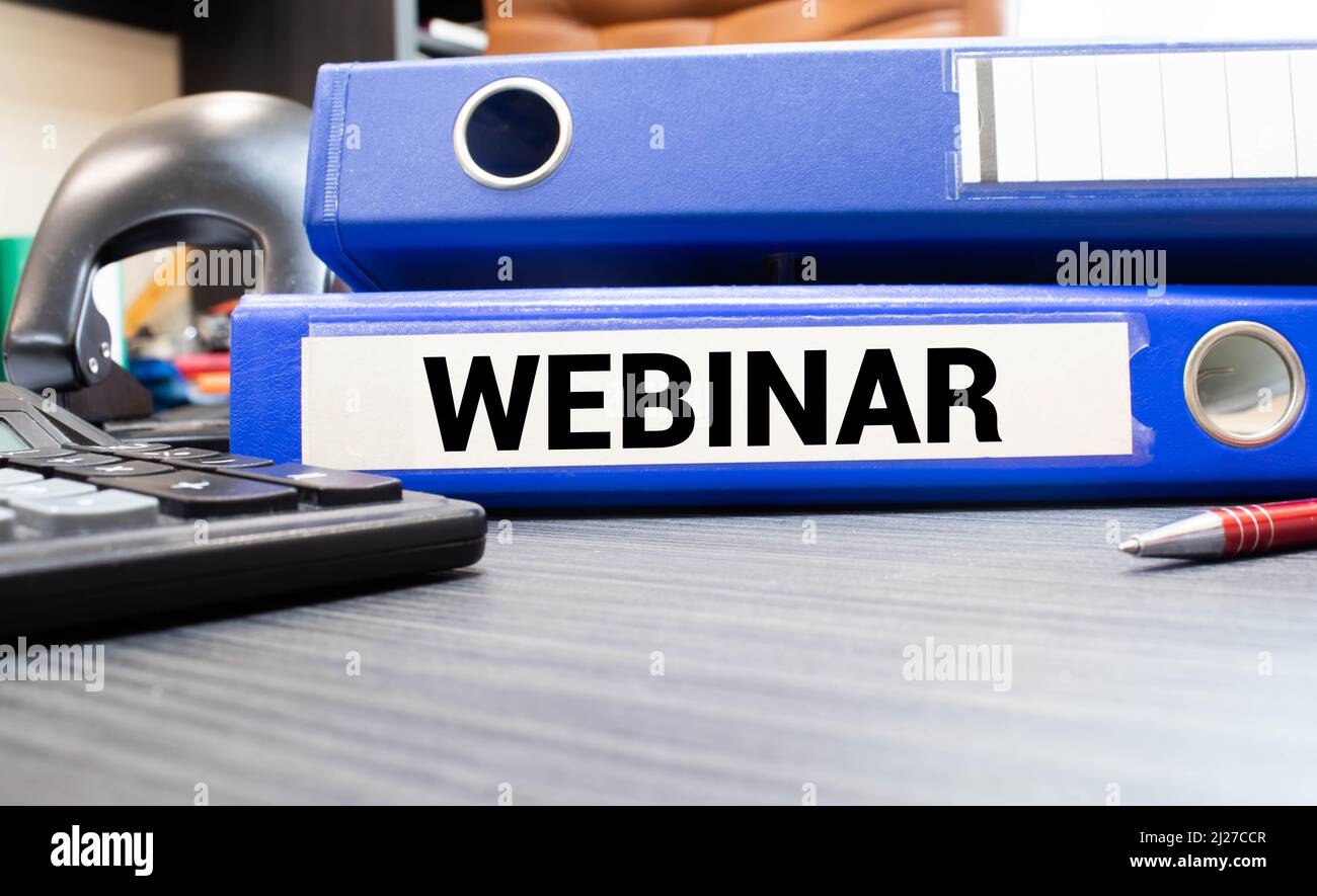 The word Webinar is written in black letters on yellow note paper. A yellow pen is embedded in the background of the blue diary. Stock Photo