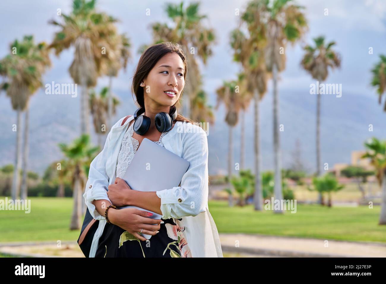 Outdoor portrait of asian female student with backpack headphones laptop Stock Photo