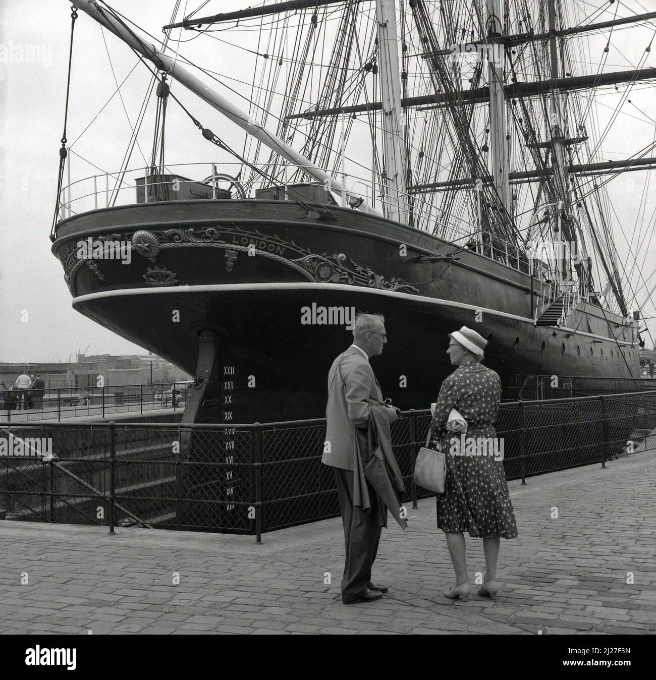 1950s, historical, a gentleman and lady standing by the rear or stern of the sailing ship, the Cutty Sark, Greenwich, London, England, UK. Built in Scotland in 1869 to carry tea back from China, the three-masted clipper ship was famous for its record-breaking passages. Stock Photo