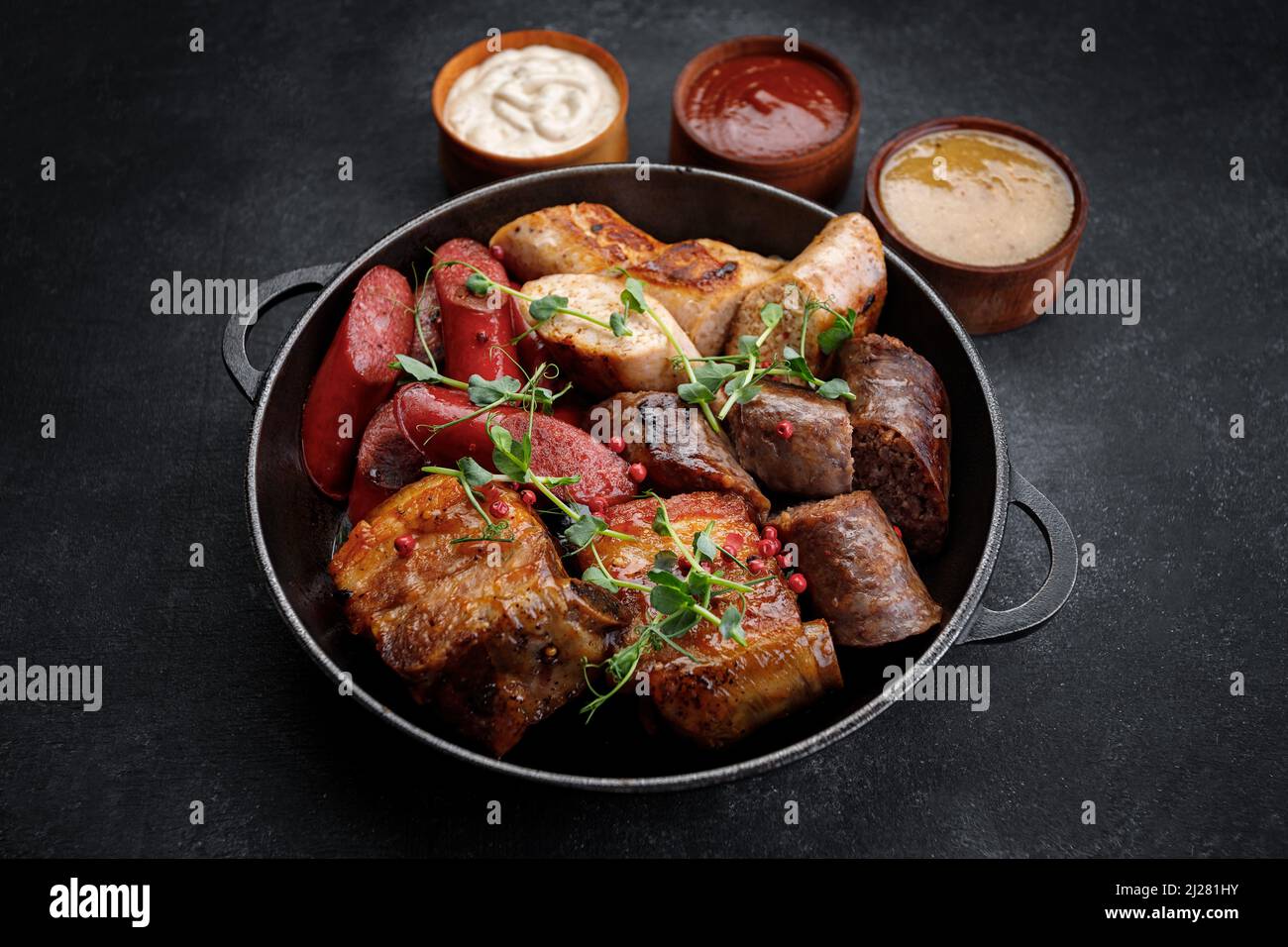 https://c8.alamy.com/comp/2J281HY/meat-fried-platter-in-a-pan-and-sauces-sausages-ribs-chicken-sausage-pork-sausage-on-a-black-background-2J281HY.jpg