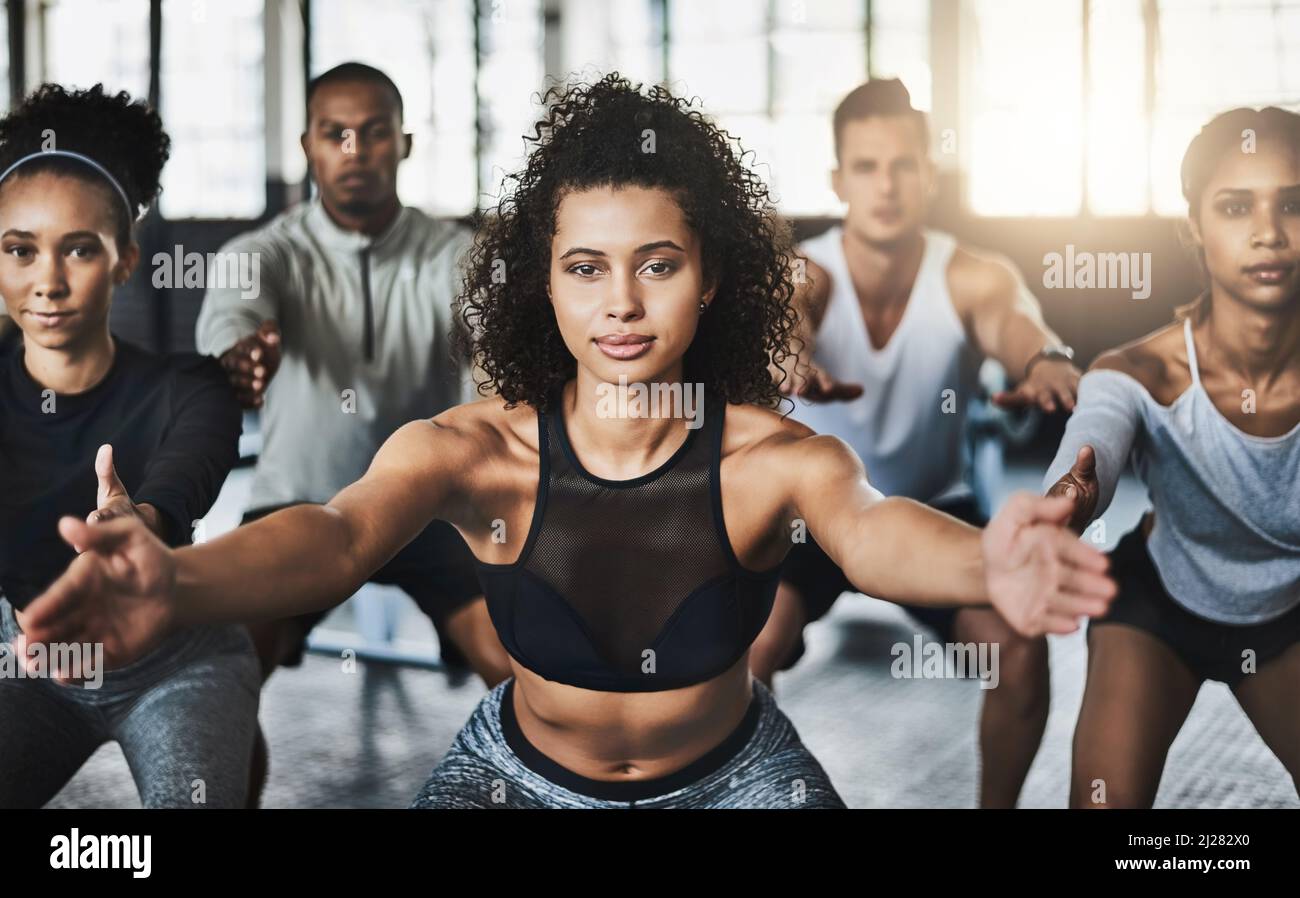 Great things happen when you clear your mind of cant. Shot of a group of young people doing squats together during their workout in a gym. Stock Photo