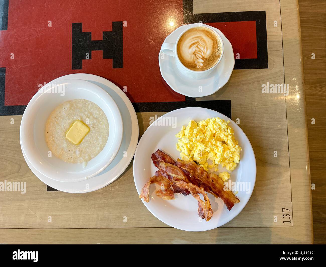 A delicious breakfast consisting of scrambled eggs, bacon, grits and a cup of cappuccino served on a cruise ship. Stock Photo