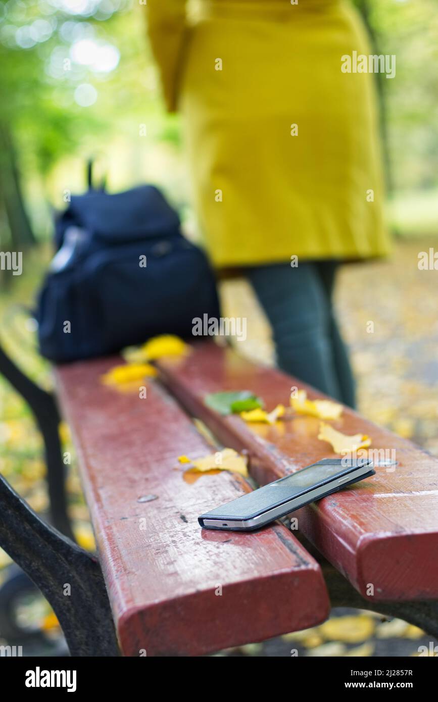 Forgotten smartphone on a park bench. Woman is leaving from a bench where she lost her cell phone. Stock Photo
