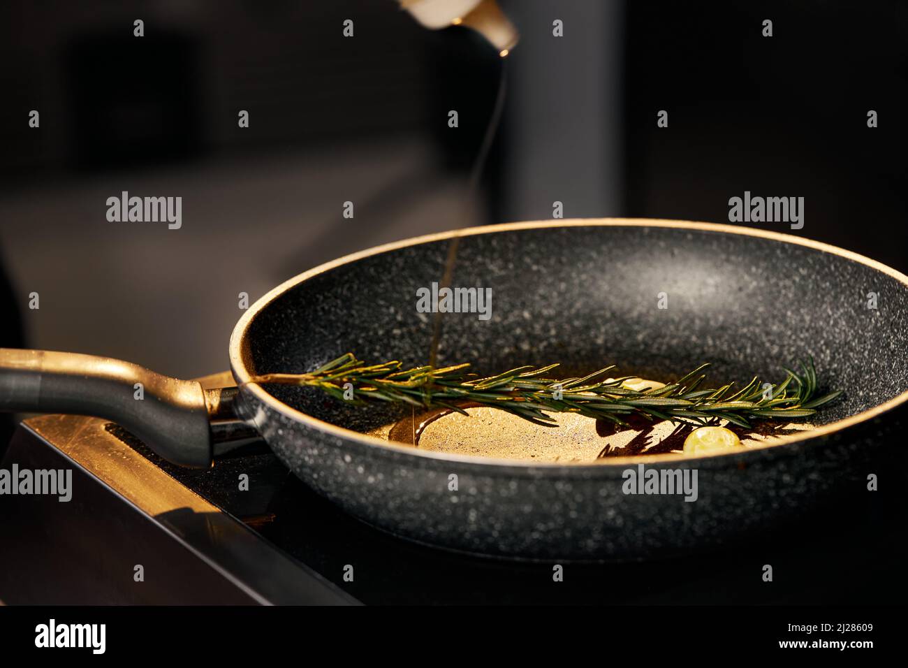 Close view of green, flavored rosemary stick with garlic and oil prepared for roasting. Olive oil pouring in pan with spices for frying on oven in restaurant kitchen. Concept of cooking. Stock Photo