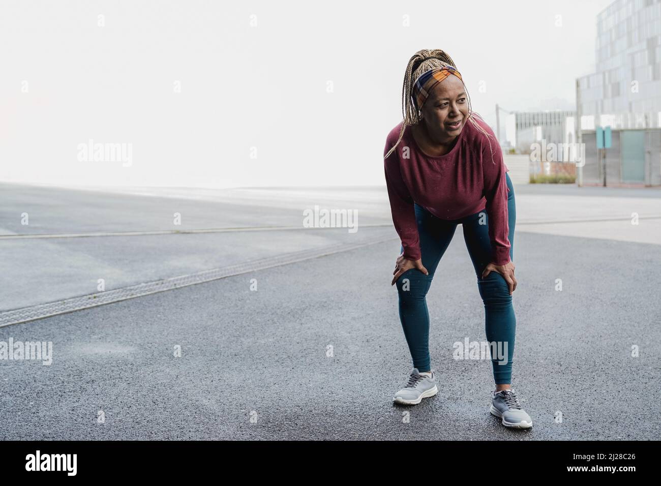 Sport senior African woman running outdoor on rainy day - Focus on face Stock Photo