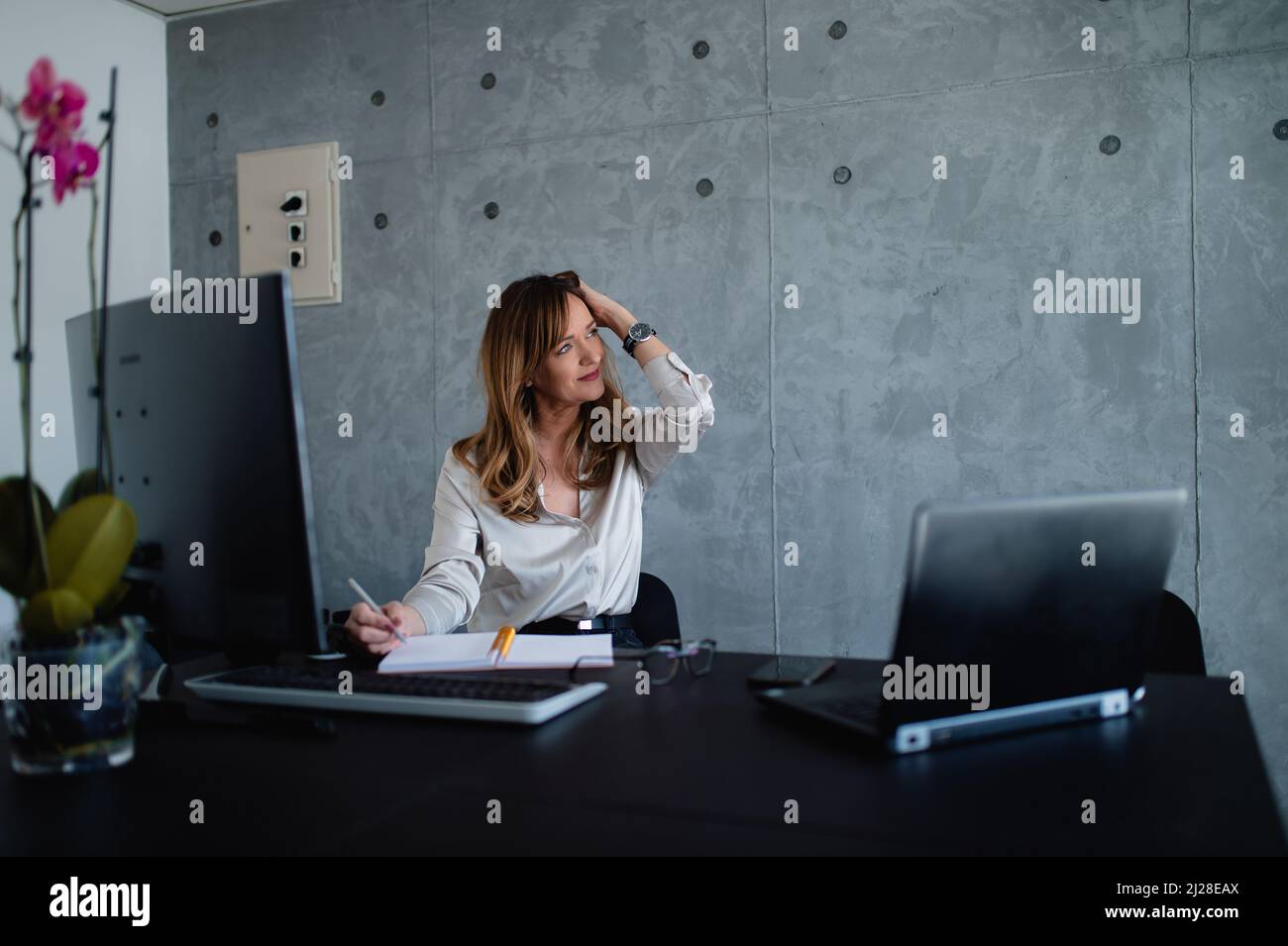 The Caucasian woman lawyer is in grey interior office, she is relaxing before her important meeting in a pleasant big corporation. Stock Photo