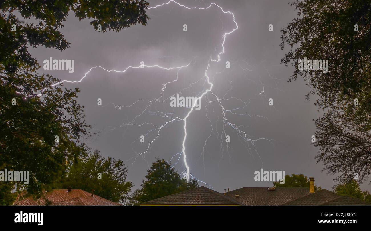 A flash of lightning in the gray sky above the roofs of houses Stock