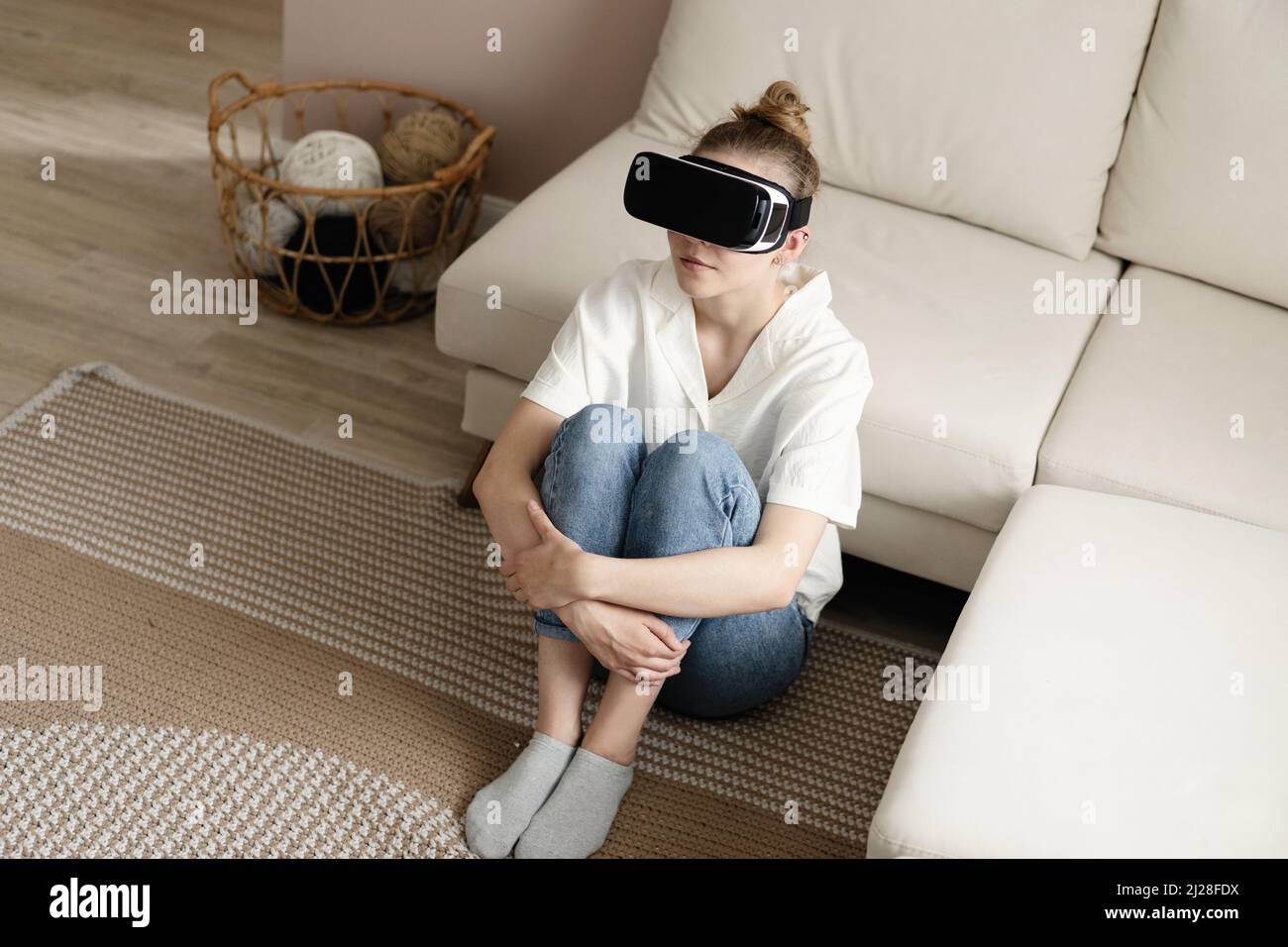 Testing new technologies. Attractive young woman in VR headset gesturing and smiling while sitting at home. Woman in VR headset looking up at the obje Stock Photo