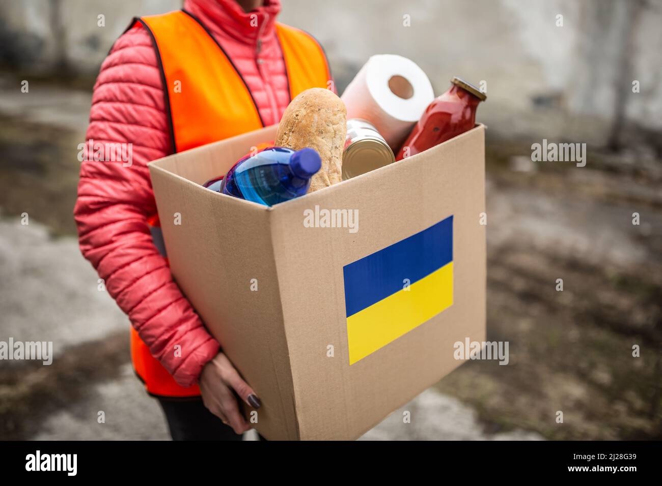 NGO volunteer carries a box with basic food and toilet papier with a Ukrianian flag sticker on the cardboard. Stock Photo