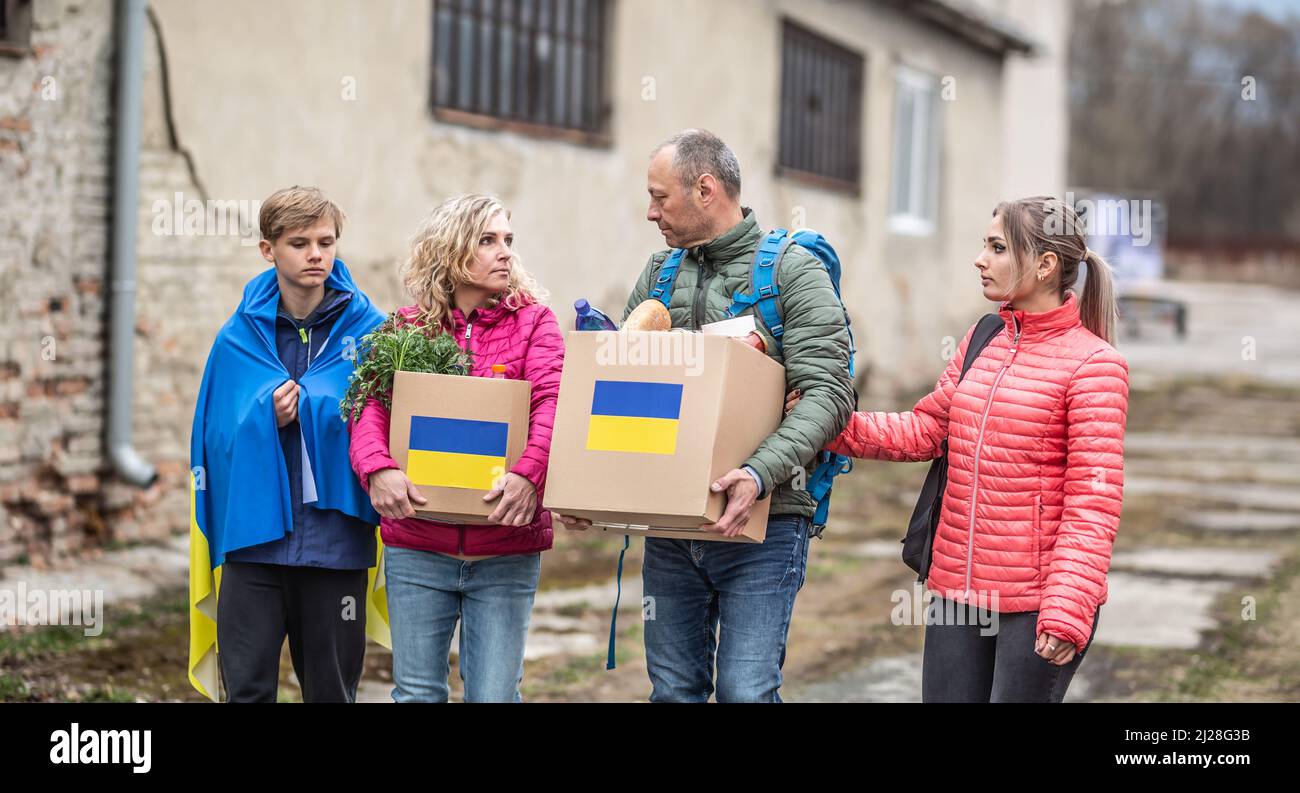 Husband, wife and two teenage kids carry boxes marked with Ukrainian flag filled with humanitarian aid in the conflict zone during war. Stock Photo