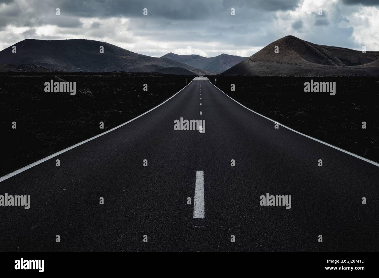 Endless road on a volcano in Timanfaya National Park in Lanzarote in the Canary Islands with a continuous line, black volcanic rocks on the side and Stock Photo