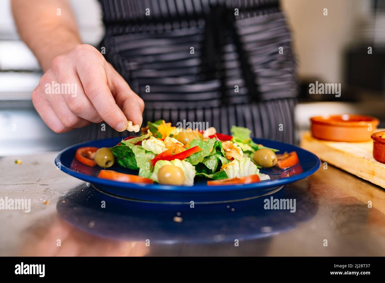 Detail of the hands of a young boss, putting ingredients on a salad plate in a professional kitchen. Stock Photo