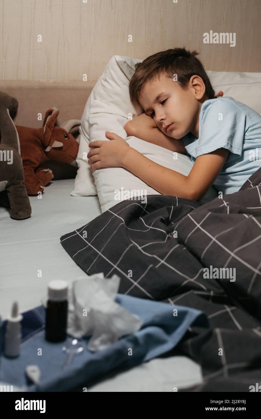 Tired ill child laying in bed with toys and tablet Stock Photo